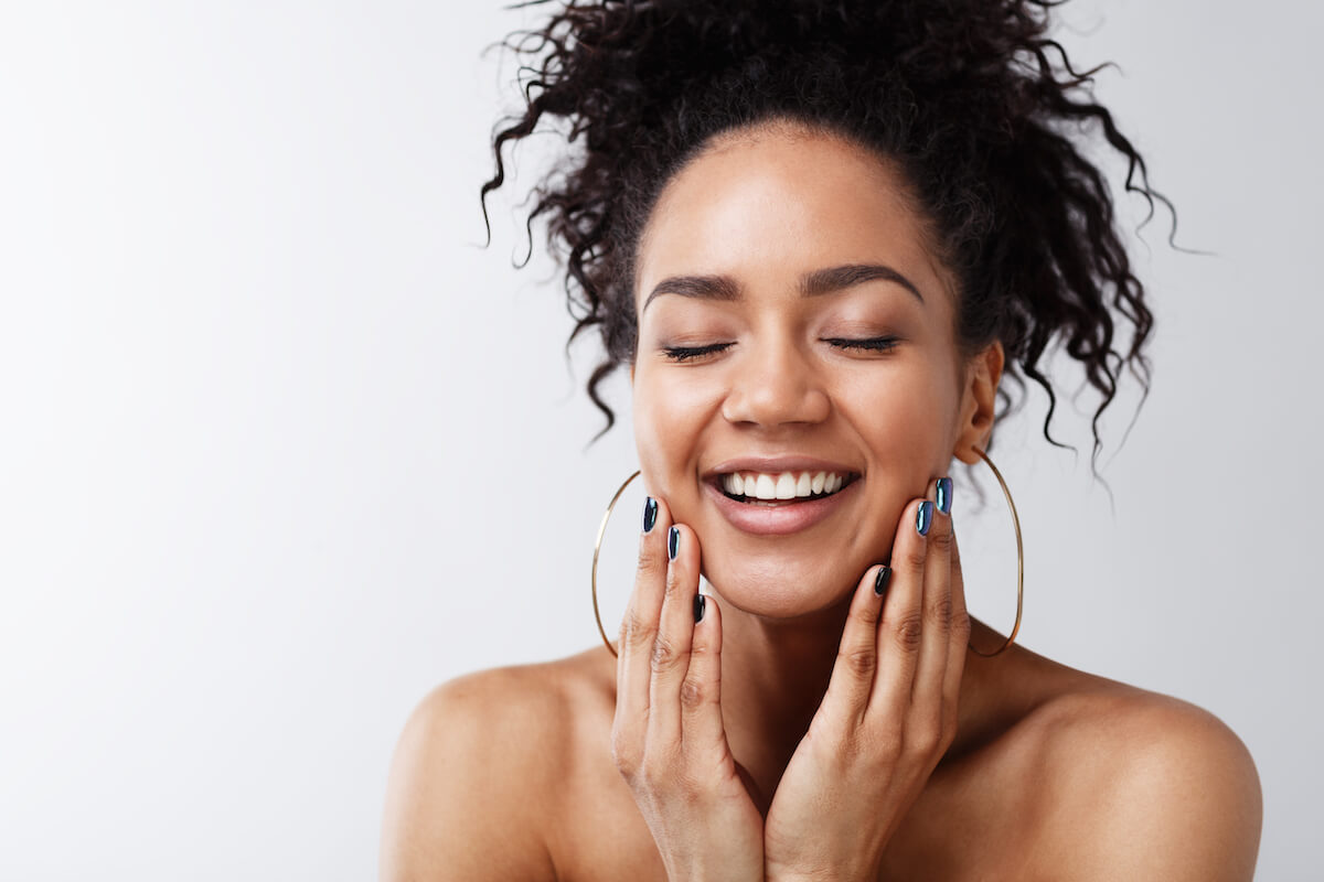 woman with eyes closed touching face