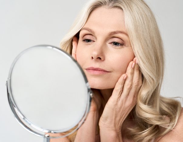 Closeup portrait of gorgeous happy middle age woman looking at mirror touching her skin enjoying treatment for dry skin. Advertising of antiaging beauty skin care products.